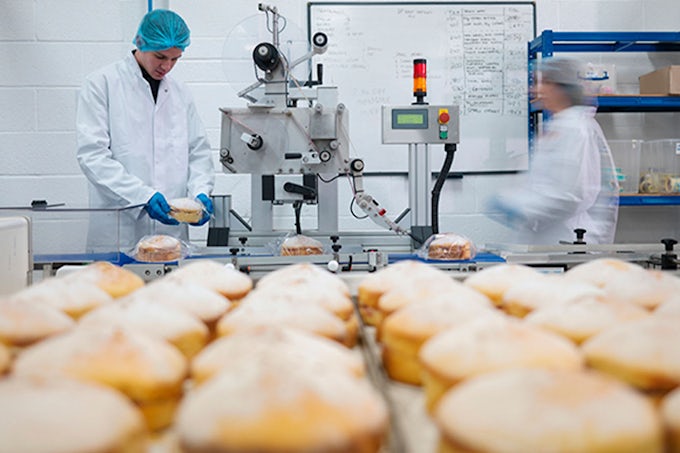 Entorno de producción alimentaria industrial con trabajadores y cinta transportadora de alimentos.
