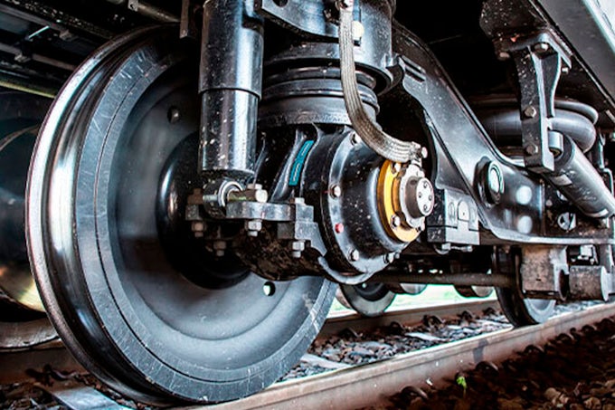 Primer plano de las ruedas de un tren, mostrando su estructura metálica robusta y los detalles del sistema de suspensión. Las ruedas de acero descansan sobre los rieles, con signos de uso visibles en su superficie.