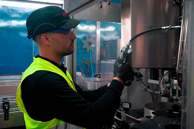 Técnico de Interflon lubricando una tetilla de engrase con una pistola y el G-Coupler. Va totalmente equipado con los elementos de seguridad: gafas, casco en forma de gorra y gafas.