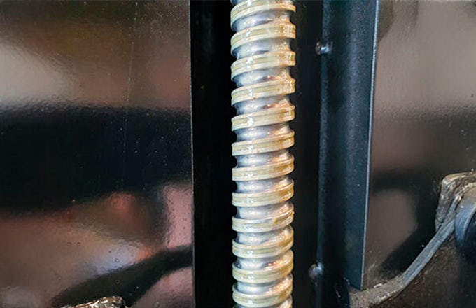 Primer plano de un husillo metálico después de ser limpiado y lubricado. Su superficie brilla con un ligero reflejo del lubricante